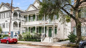 A two-story white building with green shutters, a balcony, and a front door. - The Gardenia House | Unit A | Sleeps 7 (Charleston)