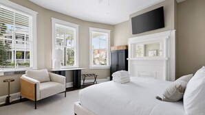 A hotel room with a large bed, a chair, a TV, and a fireplace. - The Gardenia House | Unit A | Sleeps 7 (Charleston)