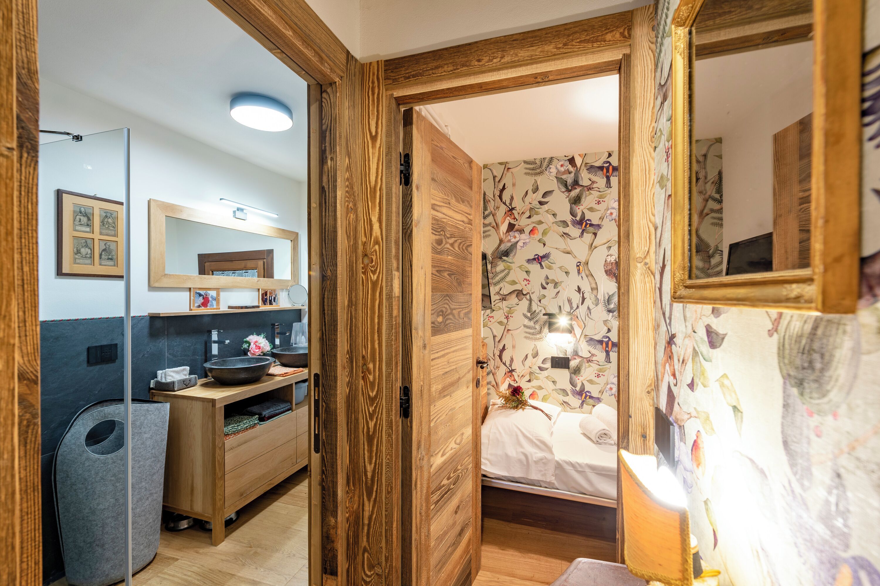 A bedroom with a wooden door, a bed with white bedding, a nightstand, and a wall with floral wallpaper.