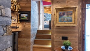 Una escalera de madera con un muro de piedra a un lado y una puerta de madera con un cuadro enmarcado al otro.
