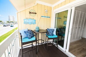 Een balkon met rieten stoelen, een tafeltje en een glazen deur die naar een kamer leidt.