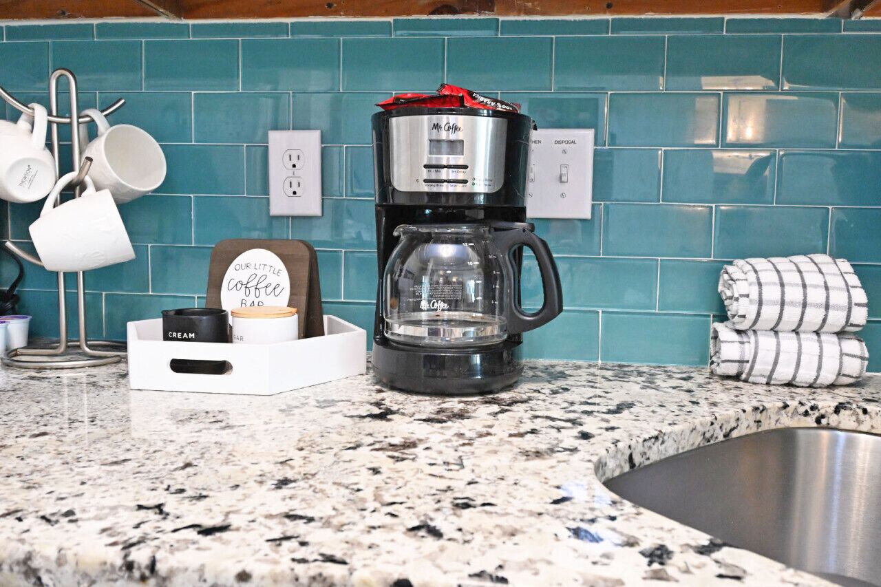 Une cuisine équipée d’une machine à café, d’un espace dédié à la préparation du café et d’un dosseret carrelé.