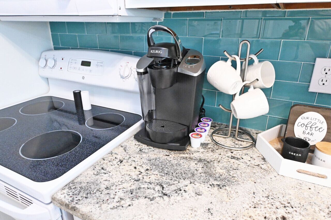 A kitchen with a Keurig coffee maker, a white stove, and a coffee cup holder with mugs.