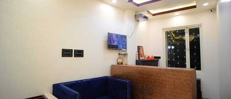 A modern living room with a blue sofa, a ceiling fan, recessed lighting, a TV, and a window with string lights.
