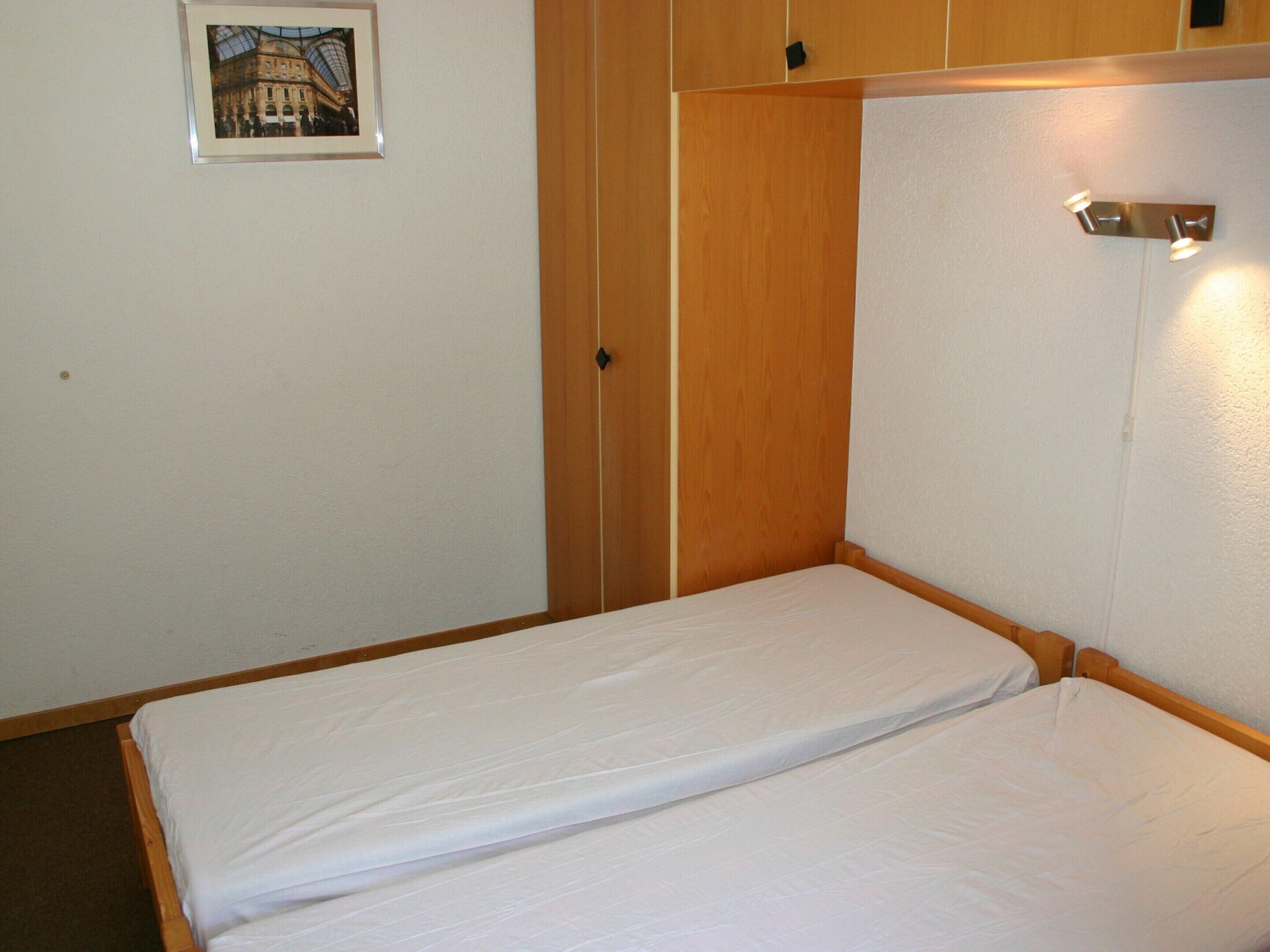 A small, single-bed room with wooden walls and a framed picture on the wall.