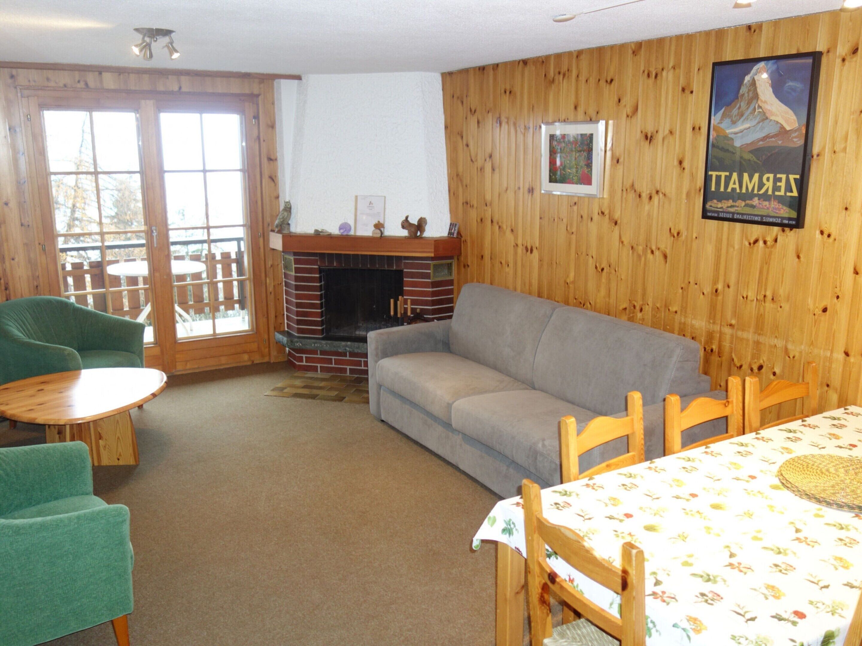 A cozy living room with a fireplace, a sofa, a dining table with chairs, and a wooden wall with a poster.