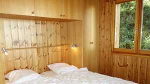 Una habitación de madera con una cama, dos lámparas de noche y un ventanal.