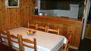 Un comedor con paneles de madera, un mantel blanco, una cesta de frutas y sillas de madera.