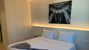 A neatly made bed with white linens and a gray throw blanket, a nightstand with a remote control, and a wall-mounted artwork depicting a staircase. - Hotel Areosa (Maia)