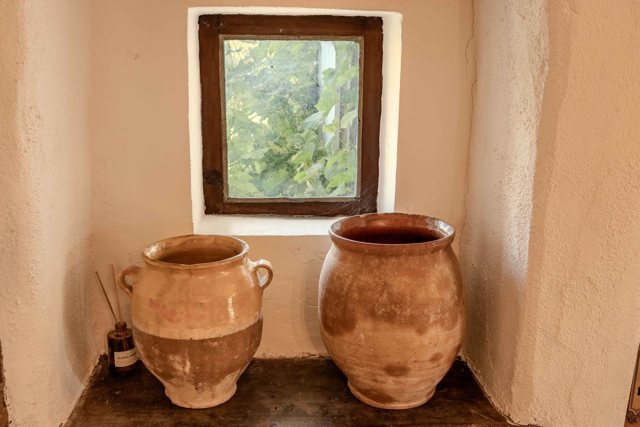 Two clay pots on a shelf next to a window with a view of greenery.