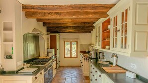 A kitchen with a tiled floor, wooden ceiling beams, white cabinetry, and a window with a view of trees. - La Ferme, Gîtes for 8 people (Puycalvel)