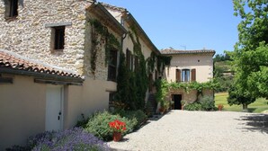 A stone building with a gravel driveway and a garden with flowers. - La Ferme, Gîtes for 8 people (Puycalvel)