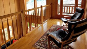 Een houten hut met een balkon, twee leren stoelen en een kamerbreed tapijt.