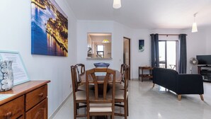 Uma sala de estar moderna com área de jantar, uma pintura grande na parede e uma TV de tela plana.