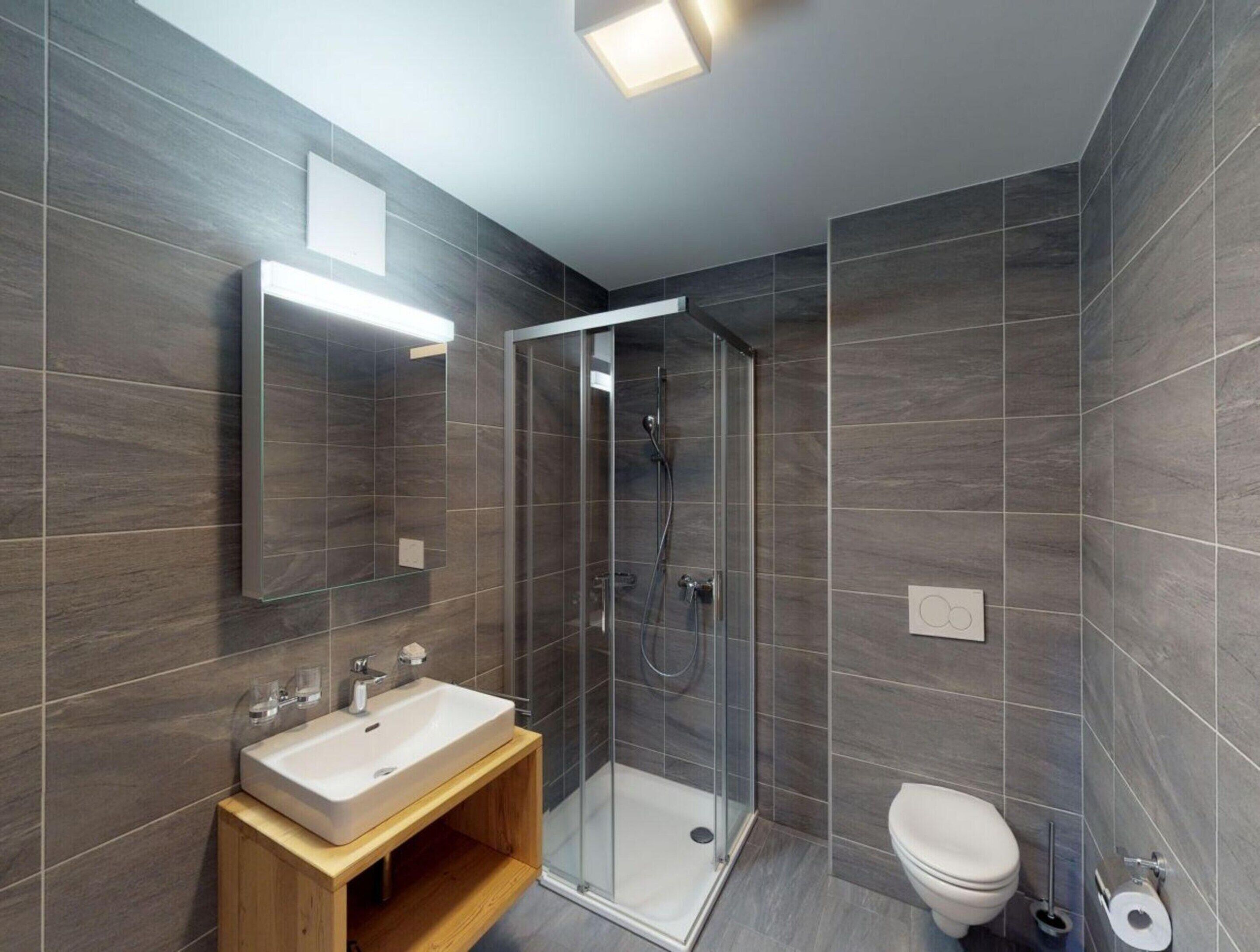 A modern bathroom with a glass-enclosed shower, a wooden vanity with a sink, and a toilet.