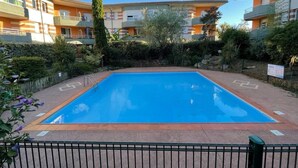 A rectangular swimming pool with a surrounding fence, surrounded by greenery and buildings in the background. - Montaigne - Proche Tram - 5min Aéroport (Blagnac)