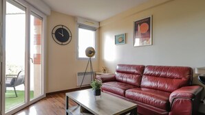 A living room with a red leather sofa, a wooden coffee table, a clock, a floor lamp, and a poster on the wall. - Montaigne - Proche Tram - 5min Aéroport (Blagnac)