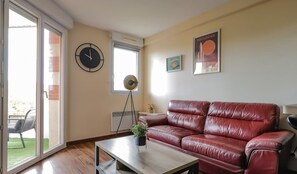 Una sala de estar con un sofá de cuero rojo, una mesa de centro de madera, un reloj, una lámpara de pie y un cartel en la pared.