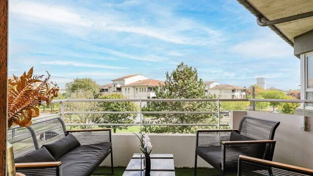A balcony with a sofa and chairs, a table, and a view of houses and greenery. - Montaigne - Proche Tram - 5min Aéroport (Blagnac)