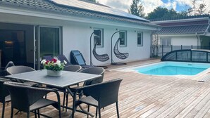 Eine Holzterrasse mit Pool, Gartenmöbeln und einem Gebäude mit weißer Fassade und schwarzen Verzierungen.