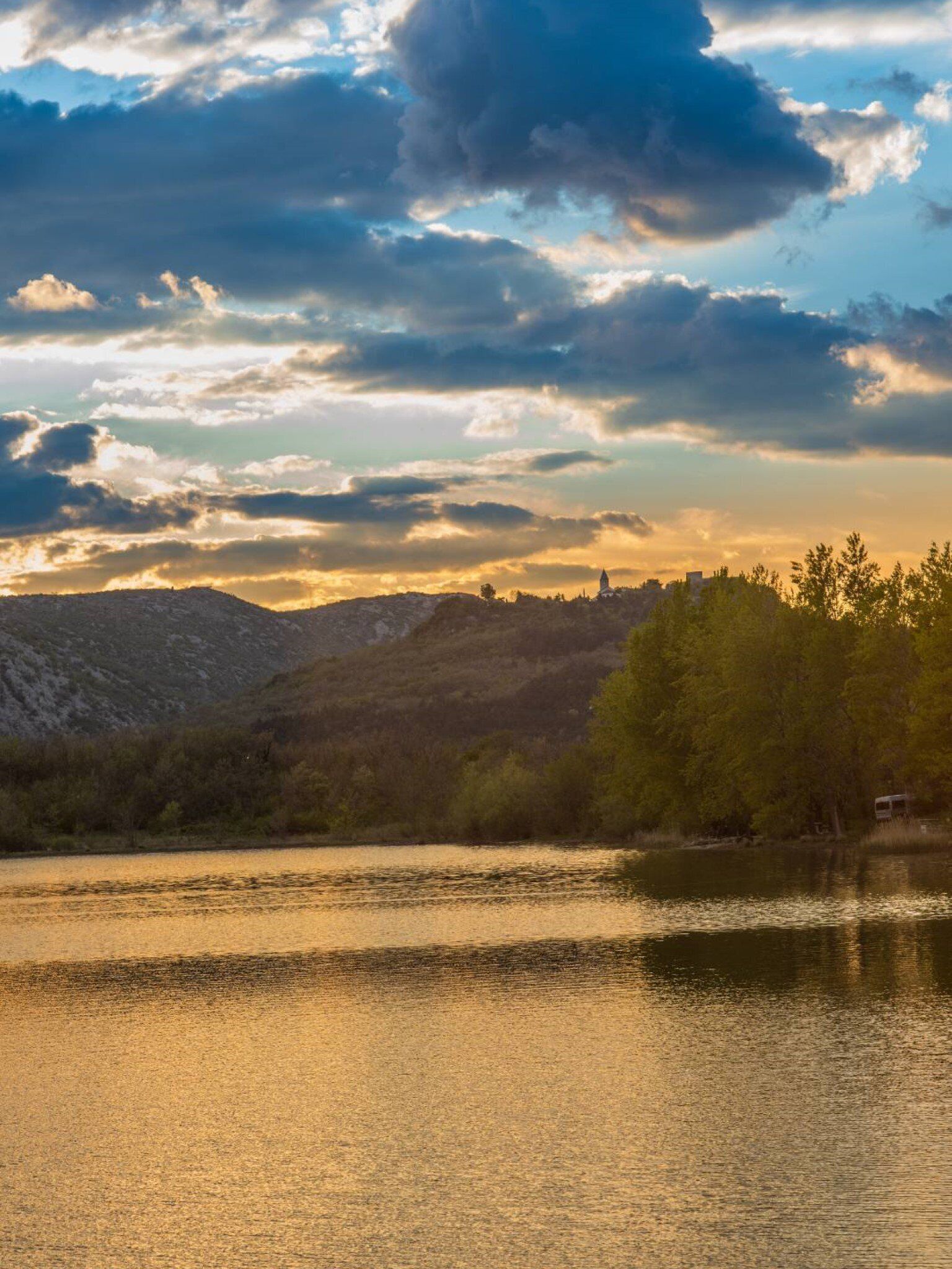 Un lago con una skyline sullo sfondo, circondato da colline e alberi.