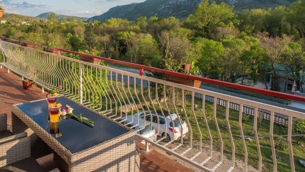 Un balcon avec vue sur une montagne, une voiture garée en contrebas et une table avec des boissons et des fleurs.