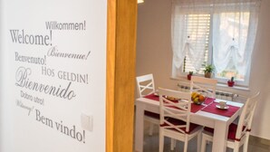 Un coin repas avec une table et des chaises blanches, un set de table rouge et une fenêtre avec des rideaux.