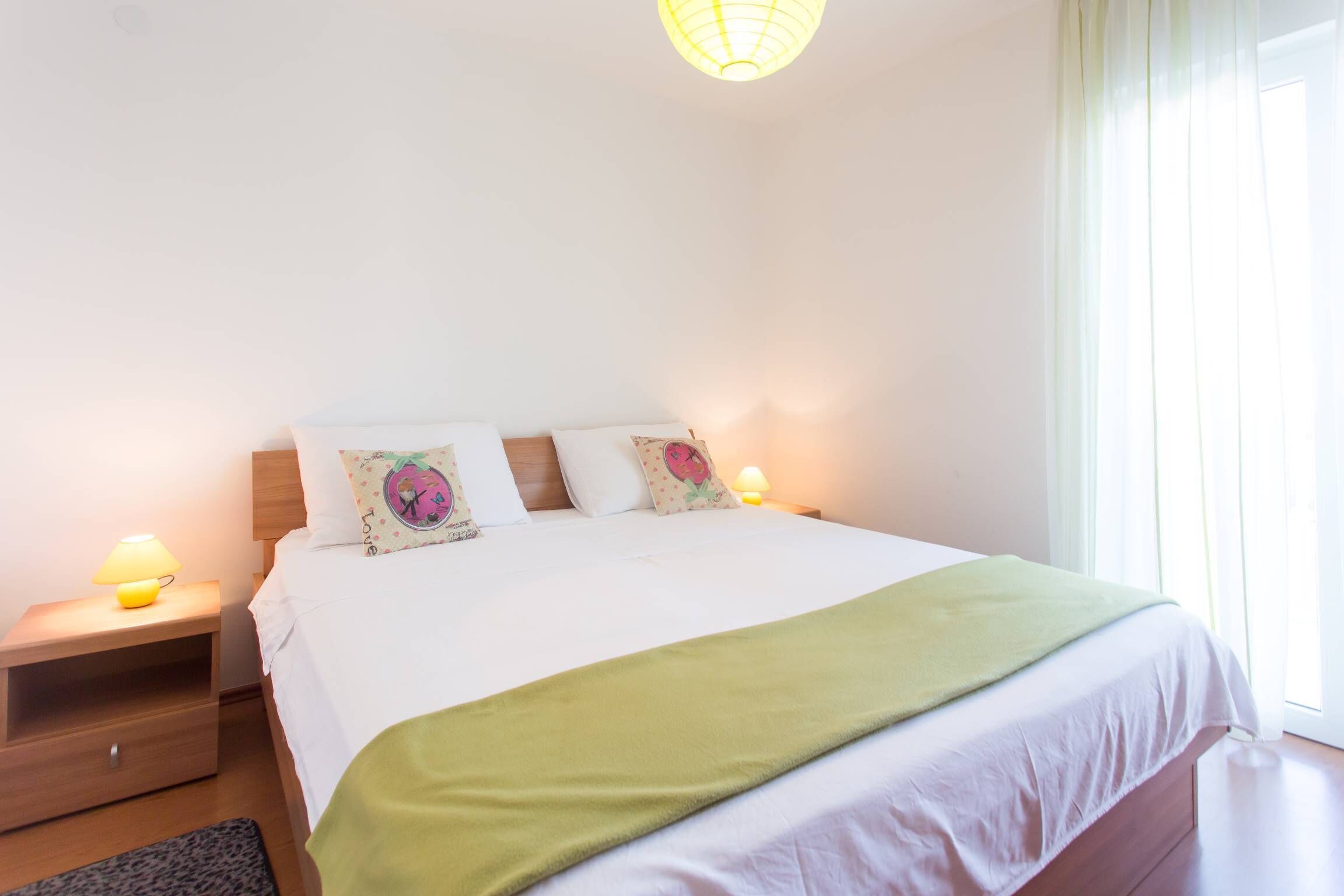 A neatly made bed with a green blanket, two bedside lamps, and a nightstand with a lamp.