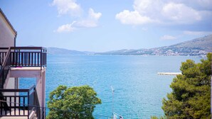 Ένα μπαλκόνι με θέα σε μια ήρεμη θάλασσα, με μακρινά βουνά και έναν καθαρό ουρανό.