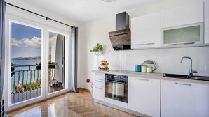Μια σύγχρονη κουζίνα με ένα μεγάλο παράθυρο, έναν εντοιχισμένο φούρνο και θέα στη θάλασσα.