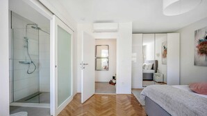 Ένα σύγχρονο υπνοδωμάτιο με ένα μεγάλο κρεβάτι, μια μεγάλη ντουλάπα και ένα ντους με γυάλινο διαχωριστικό.