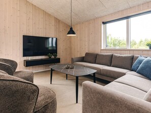 Un soggiorno moderno con una TV a schermo piatto montata su una parete in legno, un tavolino da caffè in marmo scuro, un divano grigio con cuscini blu e una lampada a sospensione.