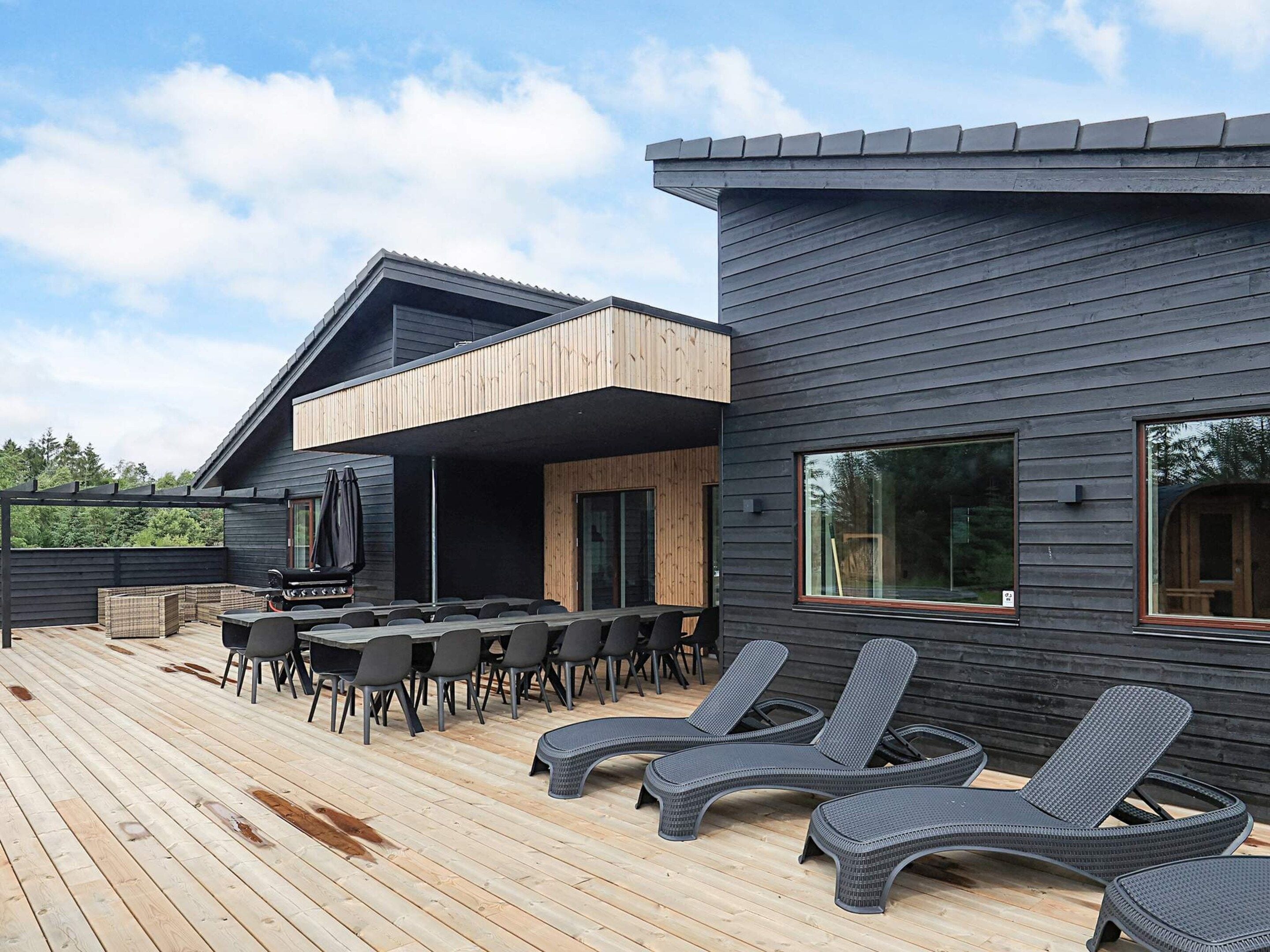A modern outdoor deck with a dining area, lounge chairs, and a barbecue setup.