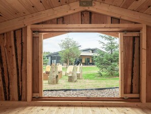 Une pièce aux murs en bois, donnant sur un espace extérieur aménagé en coin salon et sur un bâtiment situé au loin.