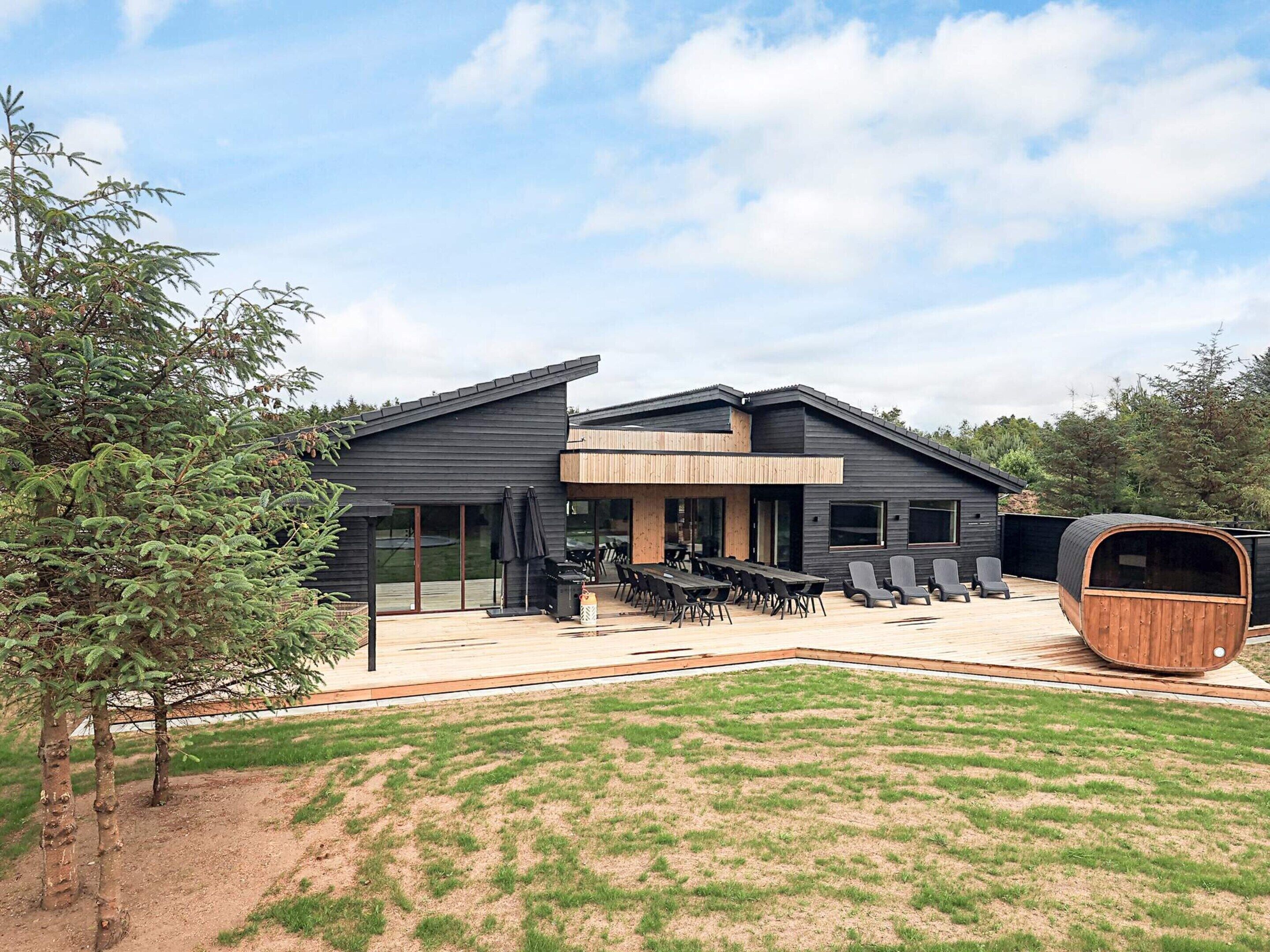 A modern house with a large deck, outdoor seating, and a sauna.