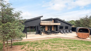 Ein modernes Haus mit einer großen Terrasse, Sitzgelegenheiten im Freien und einer Sauna.