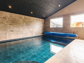 A swimming pool with a blue tint, a stone wall, and a bench. - 5 Star Holiday Home in Hojslev (Hojslev)