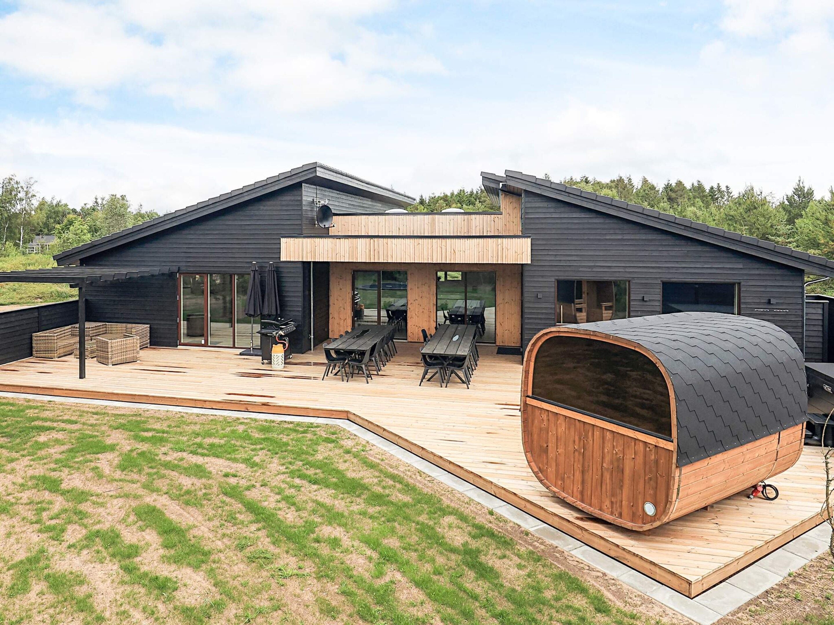 A modern house with a deck, outdoor seating, and a large barrel.