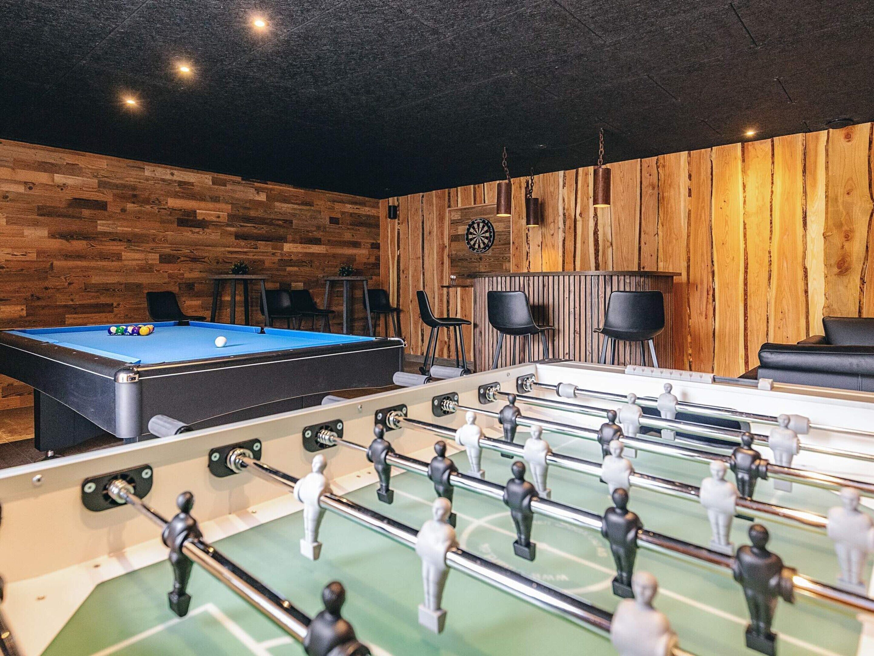 A recreational room with a pool table, foosball table, and dartboard.