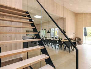 Un intérieur moderne avec un escalier en bois, un coin repas avec des chaises et des tables, et une cuisine en arrière-plan.