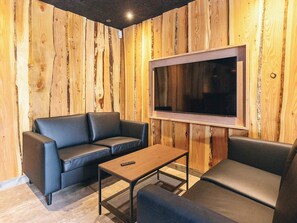Ein modernes Wohnzimmer mit einer Holzwand, einem großen Flachbildfernseher, einem schwarzen Ledersofa und einem Couchtisch.