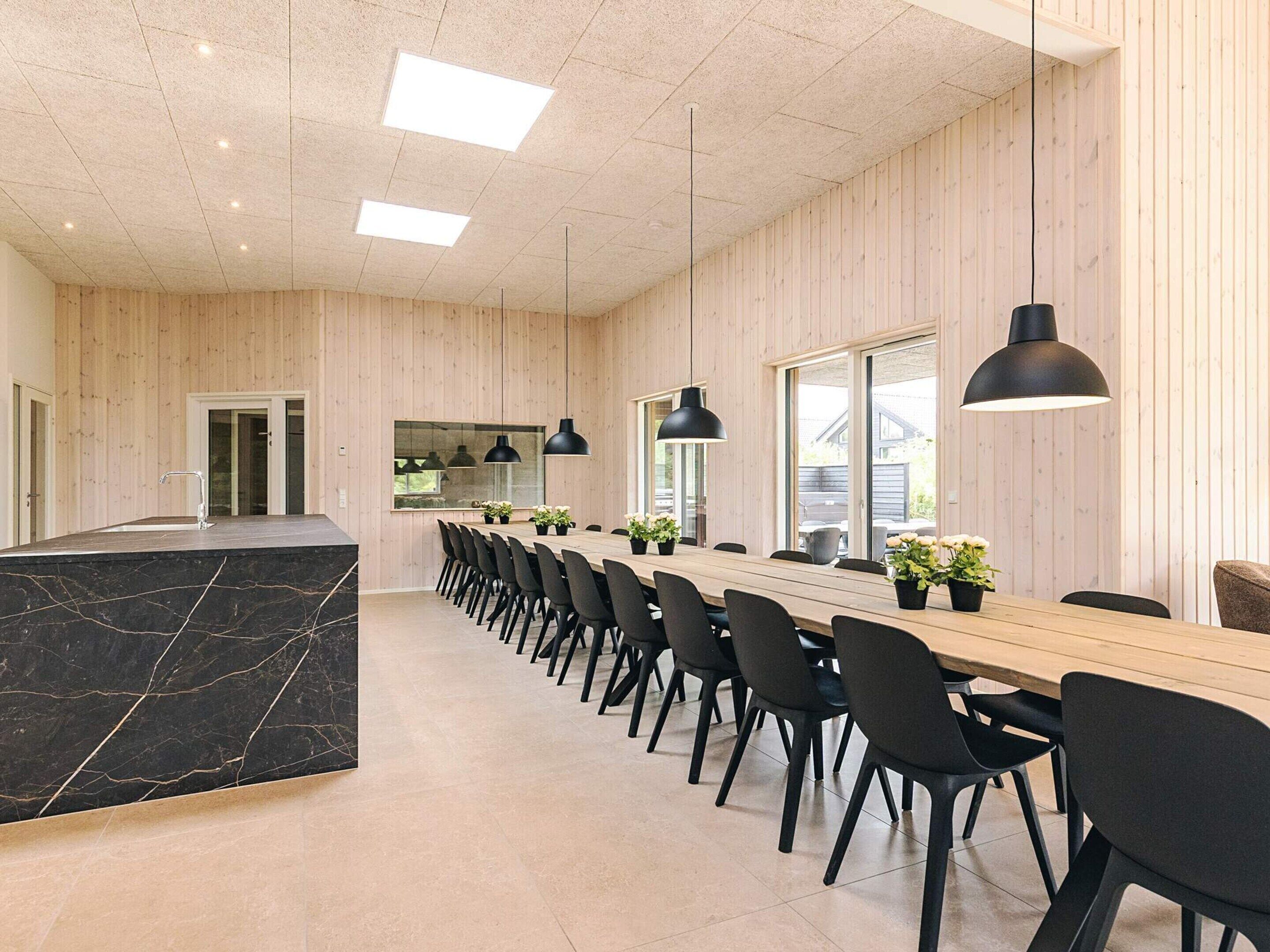 A modern dining area with a long wooden table, black chairs, and pendant lighting.