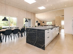 A modern kitchen with a large island, wooden walls, and large windows. - 5 Star Holiday Home in Hojslev (Hojslev)