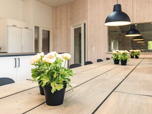 A long wooden table with black pots of flowers and a modern kitchen in the background. - 5 Star Holiday Home in Hojslev (Hojslev)