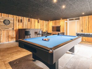 A pool table with a blue felt surface, surrounded by wooden panel walls, a dartboard, and a television on a wooden stand. - 5 Star Holiday Home in Hojslev (Hojslev)