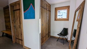 Une pièce avec des armoires en bois, un banc, une chaise et un tableau représentant une montagne.