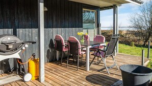 Un patio exterior con una mesa, sillas, una parrilla y un bote de basura negro.