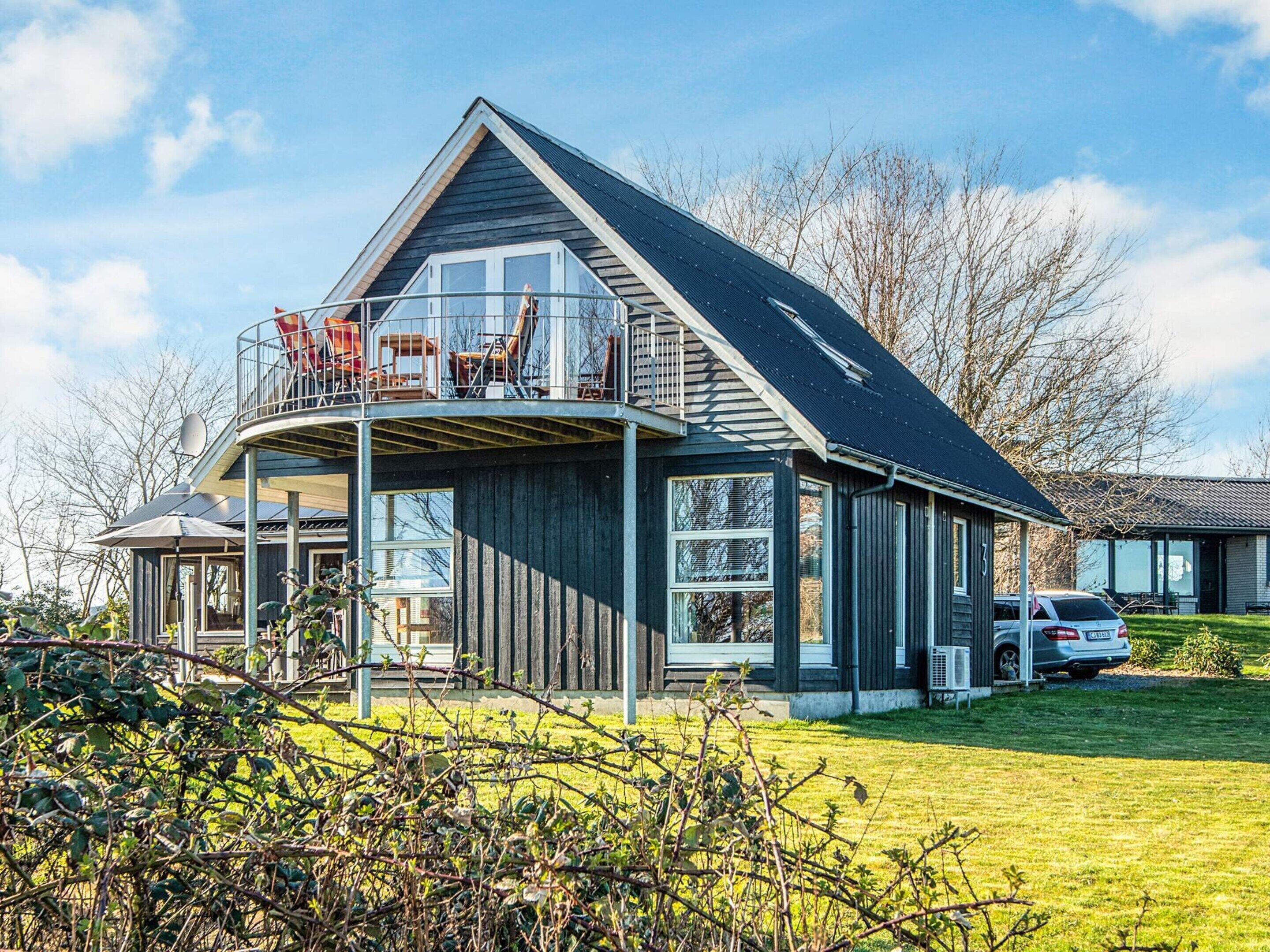 Ett modernt hus i två våningar med en balkong, stora fönster och en täckt uteplats.