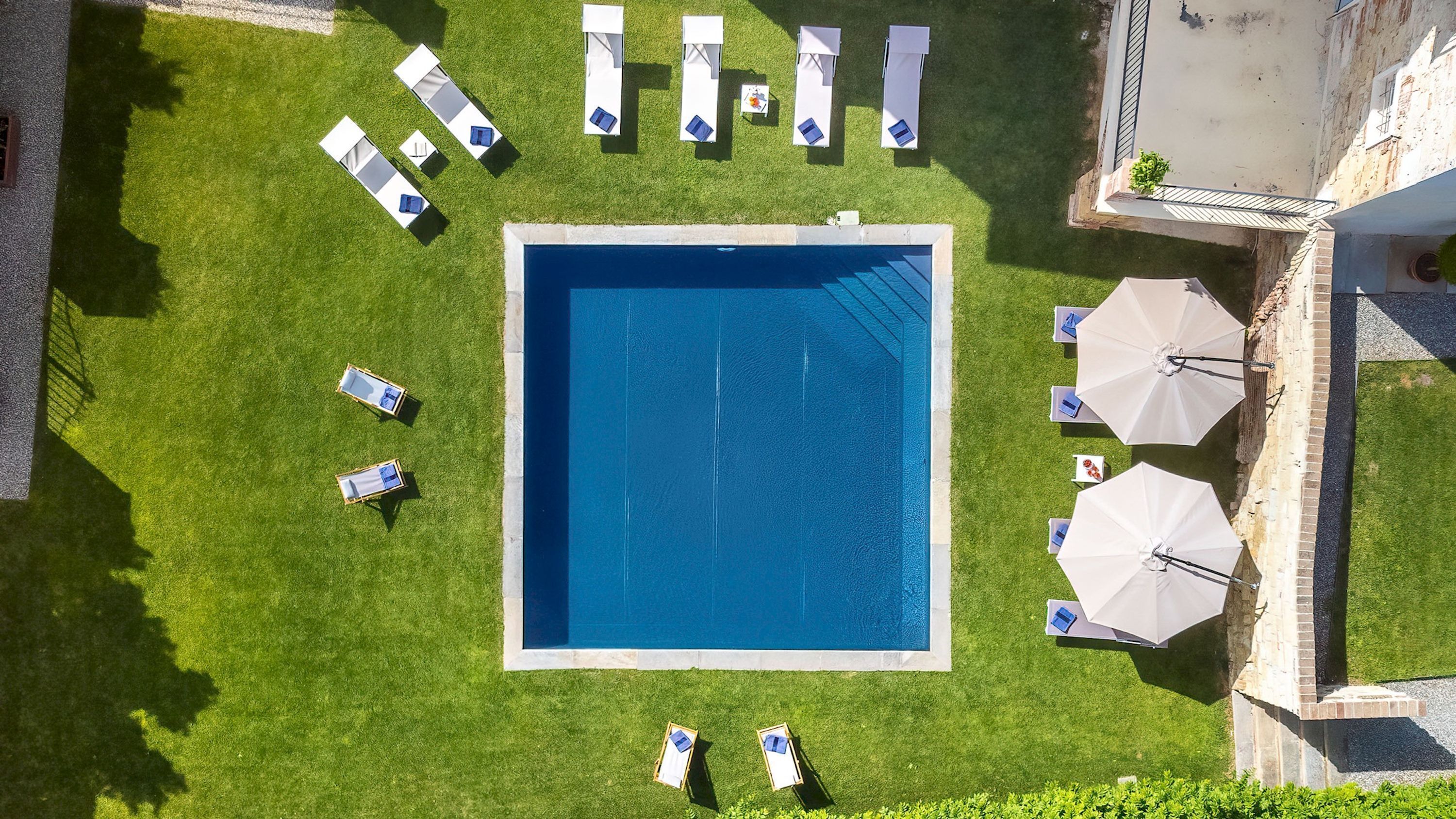 An aerial view of a swimming pool surrounded by lounge chairs and umbrellas, with a well-maintained lawn.