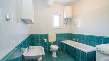 A bathroom with a toilet, bidet, bathtub, and a washing machine.